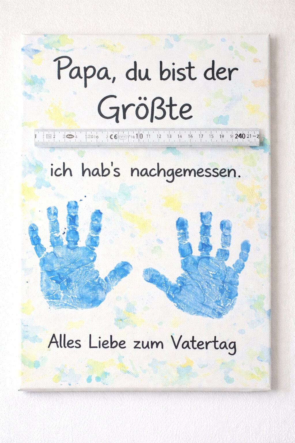 Leinwand mit blauen Handabdrücken, Zollstock und Spruch „Papa, du bist der Größte“ zum Vatertag.
