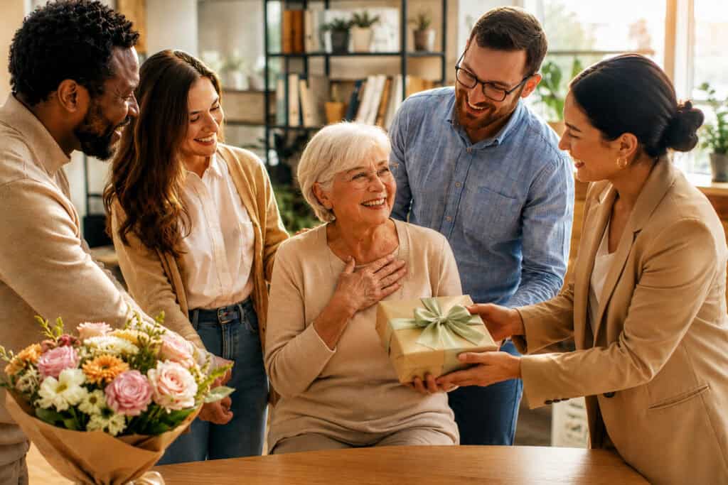 Kolleginnen und Kollegen überreichen einer Frau zum Ruhestand ein Geschenk und einen Blumenstrauß.