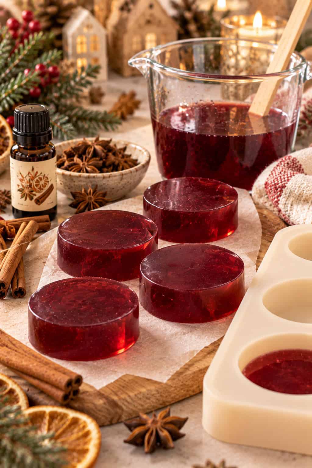 Selbstgemachte Glühwein-Seife in tiefem Weinrot auf einem Holzbrett, daneben eine runde Silikonform, ein Glasmessbecher mit roter Seifenmasse und Glühwein-Duftöl. Zimtstangen, Sternanis und Tannenzweige sorgen für eine weihnachtliche Atmosphäre.